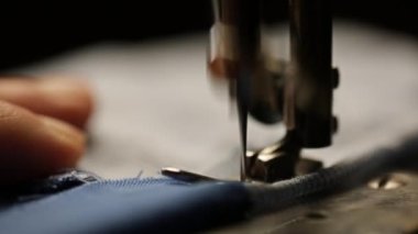 Kumaş, beyaz iplikle yakın plan bir dikiş makinesine dikilmiş.