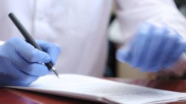 Lastik eldivenli bir doktor bir kalemle belge dolduruyor. Doktor hastanede belgelerle çalışıyor. Bir salgın sırasında çalışmak