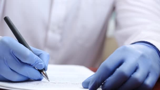 ゴム手袋の医者はペンで書類を記入します 医者は病院の書類を扱っている 病院でのパンデミックの間に働くこと — ストック動画