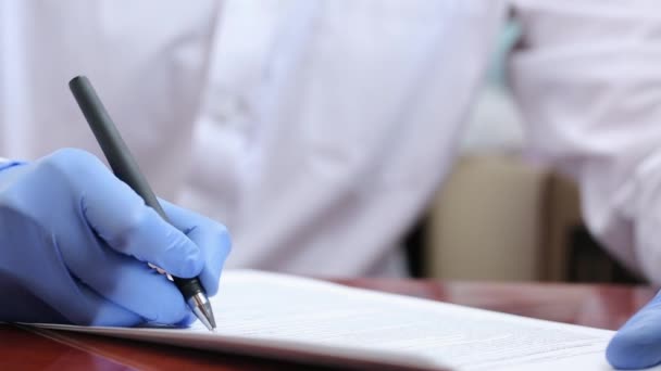 ゴム手袋の医者はペンで書類を記入します 医者は書類を扱っている パンデミックの際には — ストック動画