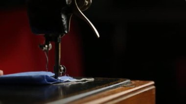 Adam eski bir dikiş makinesine mavi kumaş dikiyor.