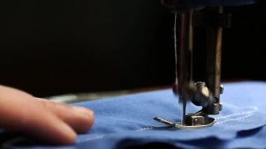 Terzi, dikiş makinesine beyaz bir iplikle diker. Mavi bir kumaş yakın plan.