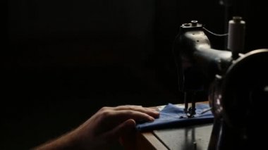 Dikiş makinesinde siyah arka planda beyaz iplikle dikiş diker.