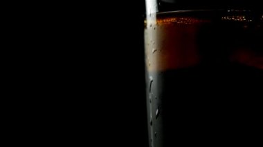 Siyah arka planda şeffaf bir cam ve buz içinde siyah karbonatlı içecek.