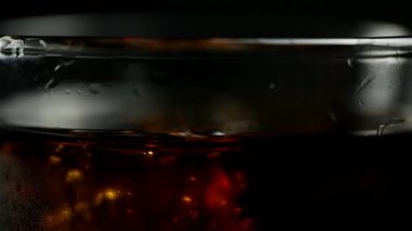 Siyah arka planda dönen viski ve buzlu bir bardak soda.