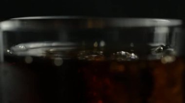 Siyah arka planda dönen viski ve buzlu bir bardak soda.
