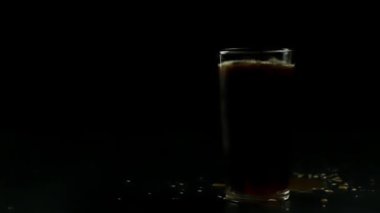 İki parça buz, siyah arka planda siyah soda ile bir bardağa düşer.