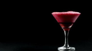 Siyah arka planda martini bardağından dökülen kırmızı köpüklü içecek.