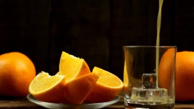 Meyve suyu buzlu bir bardağa doldurulur, bir tabakta birkaç dilim portakal ve iki bütün.