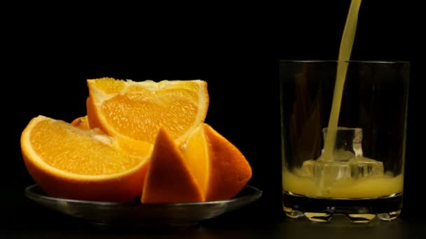 Сок Наливают Стакан Льдом Несколько Нарезанных Апельсинов Тарелке Черном Фоне — стоковое видео