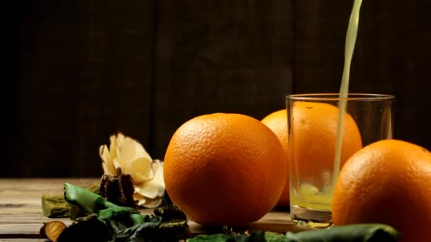 花のついたテーブルの上にオレンジジュースとオレンジ3つをグラスに注ぎます — ストック動画