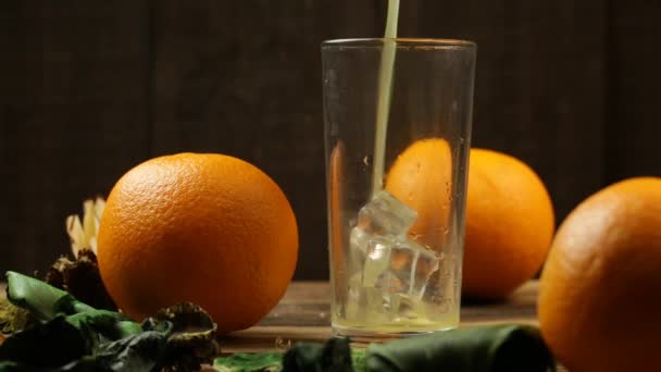 橙汁倒入装有冰块的杯子里 桔子紧靠着桌子 — 图库视频影像