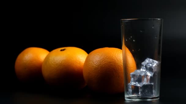 氷と背の高いガラスにオレンジジュースと3つのオレンジを注ぐ — ストック動画