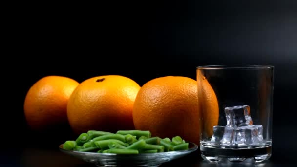 把橙汁倒入杯子里 旁边有冰块 三个橙子和豆子 — 图库视频影像