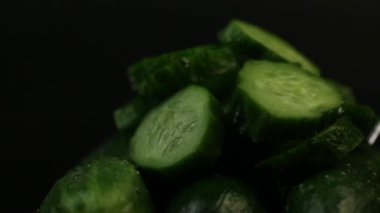 Dilimlenmiş yeşil salatalıklar siyah arka planda döner.