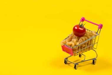 Sarı arka planda alışveriş arabasında makarna.