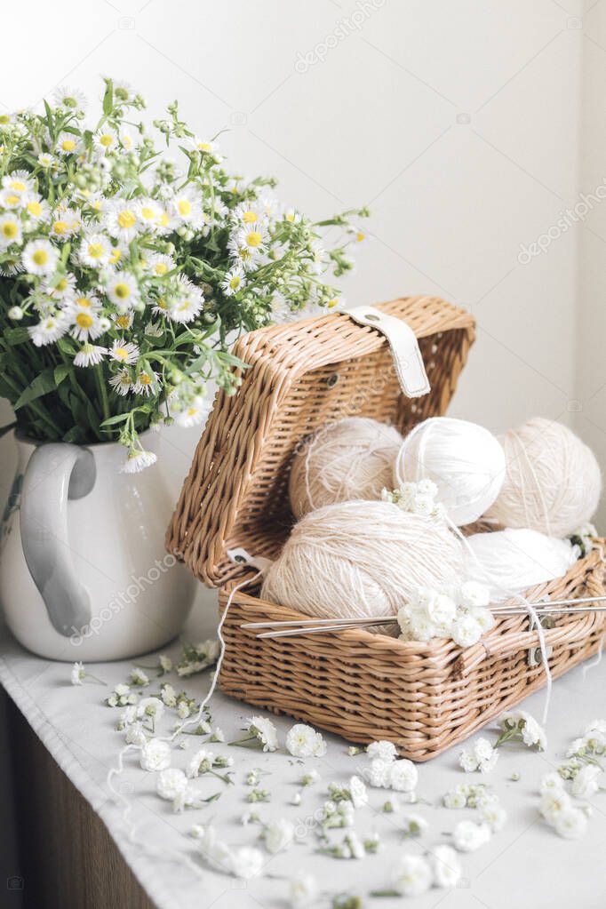 wicker basket with yarn and needles on white background. flowers in the vase