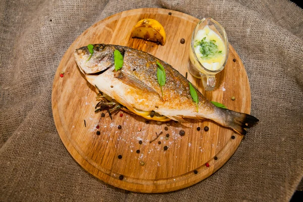 Peixe grelhado com limão e especiarias em uma tábua de madeira — Fotografia de Stock