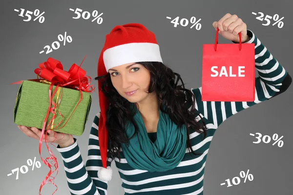 Vrouw in kerstmuts met een geschenk en verkoop tas — Stockfoto