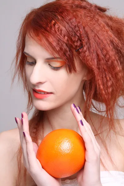 Roodharige meisje met oranje in haar handen — Stockfoto