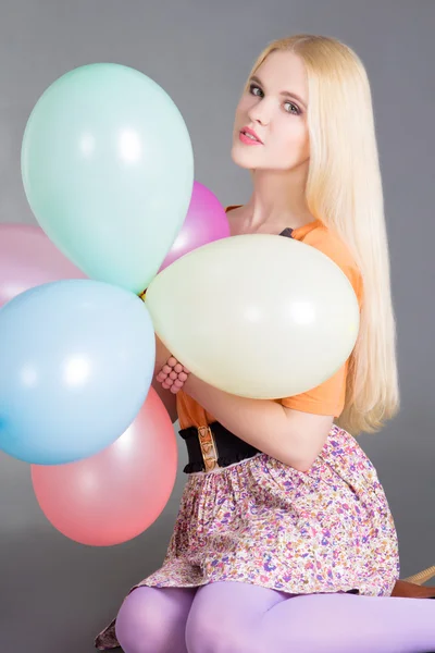 Young beautiful woman with balloons sitting over grey — Stock Photo, Image