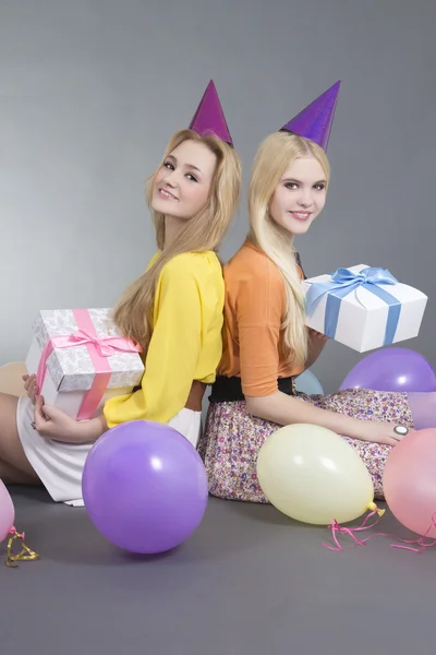 Smiling teenage girls sitting with gifts and colorful balloons — Stock Photo, Image