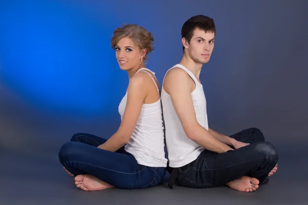 Young attractive couple sitting over blue — Zdjęcie stockowe