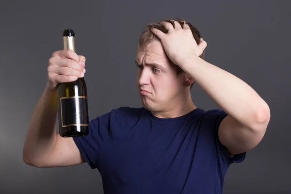 Young drunk man with bottle of champagne over grey — Stock Photo, Image