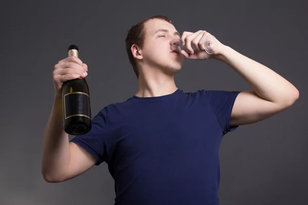 Młody człowiek pije szampana na szarym tle — Zdjęcie stockowe