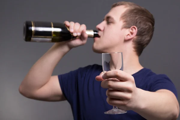 Młody człowiek, picie alkoholu na szarym tle — Zdjęcie stockowe