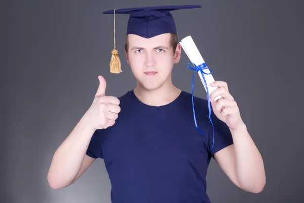 Jonge afstuderen man met diploma duimschroef opwaarts over grijs — Stockfoto