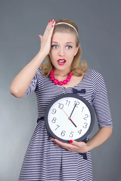Shocked pinup girl in striped dress holding the clock — Stock Photo, Image