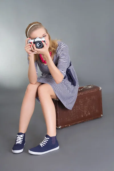 茶色のレトロなスーツケースの上に座ってカメラでピンナップの女性 — ストック写真