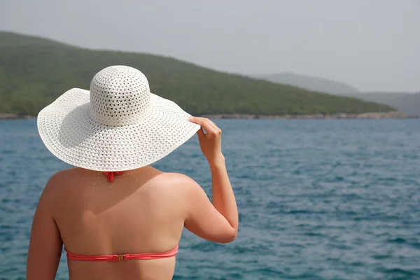 Kvinna i baddräkt och vit hatt på stranden — Stockfoto