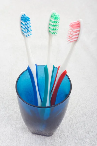 Escovas de dente em vidro azul sobre a toalha branca — Fotografia de Stock