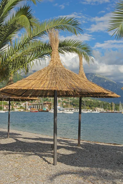 Straw sunshades and palm leafs on the beach in Montenegro — Stock Photo, Image