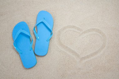 Mavi flip flop ve kumlu bir plaj üzerinde kalp