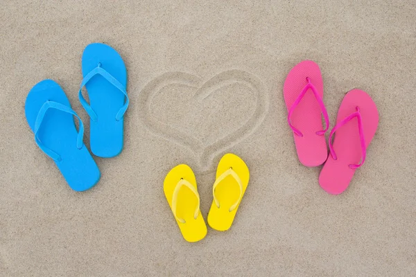 Blue, red, yellow flip flops and heart on beach — Stock Photo, Image