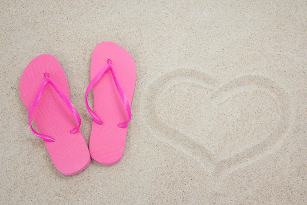 Roze flip-flops en hart op zandstrand — Stockfoto