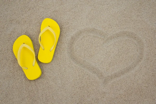 Sarı flip flop ve kumlu bir plaj üzerinde kalp — Stok fotoğraf