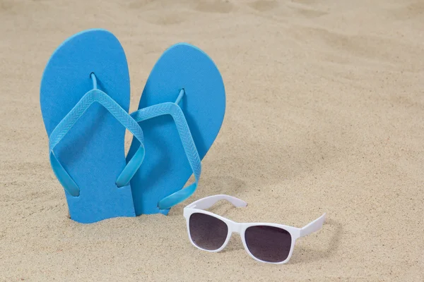 Bright blue rubber flip flops and sunglasses on the sand — Stock Photo, Image