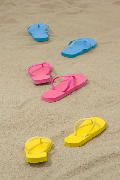 Three pairs of colorful flip flops on white sand — Stock Photo, Image