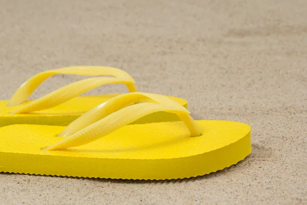 Pair of yellow flip flops on sandy beach — Stock Photo, Image