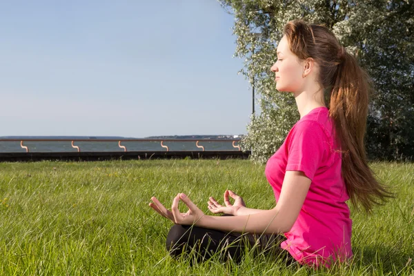Молода жінка сидить на траві в позі йоги — стокове фото
