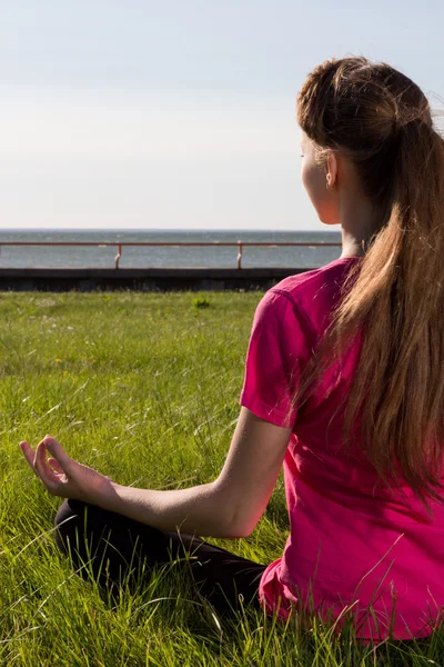 Jovem mulher siiting na grama no yoga pose — Fotografia de Stock