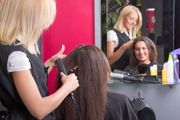 Hairdresser straightening woman's hair in beauty salon — Stock Photo, Image