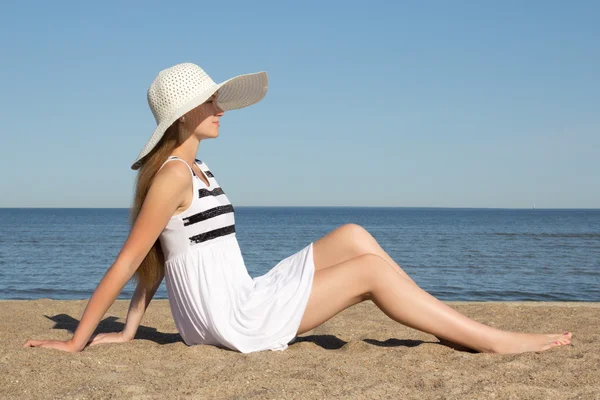 Mulher bonita no vestido listrado e chapéu sentado na praia — Fotografia de Stock