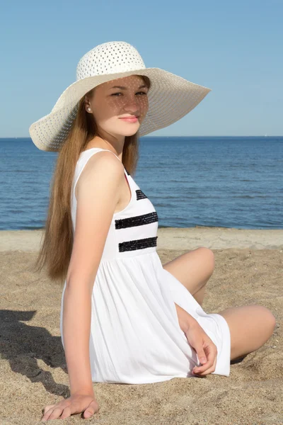 Mooie vrouw in gestreepte jurk zittend op het strand — Stockfoto