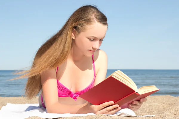 Young woman in pink bikini reading book on the beach — Photo