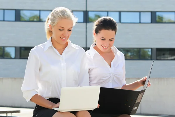 Twee zakelijke vrouwen zitten met laptop en map over straat ba Stockafbeelding